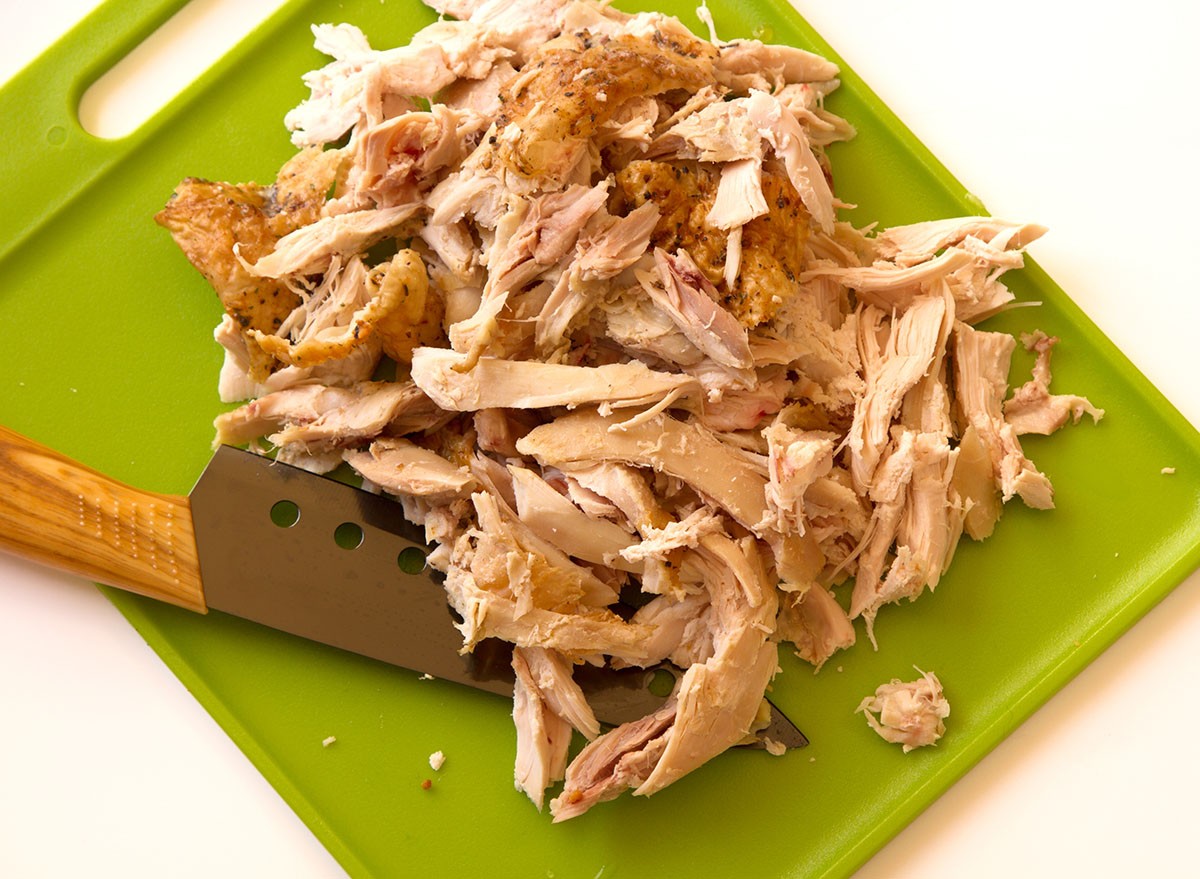 Shredded rotisserie chicken on a green cutting board and carving knife isolated on a white background with room for text or copy space