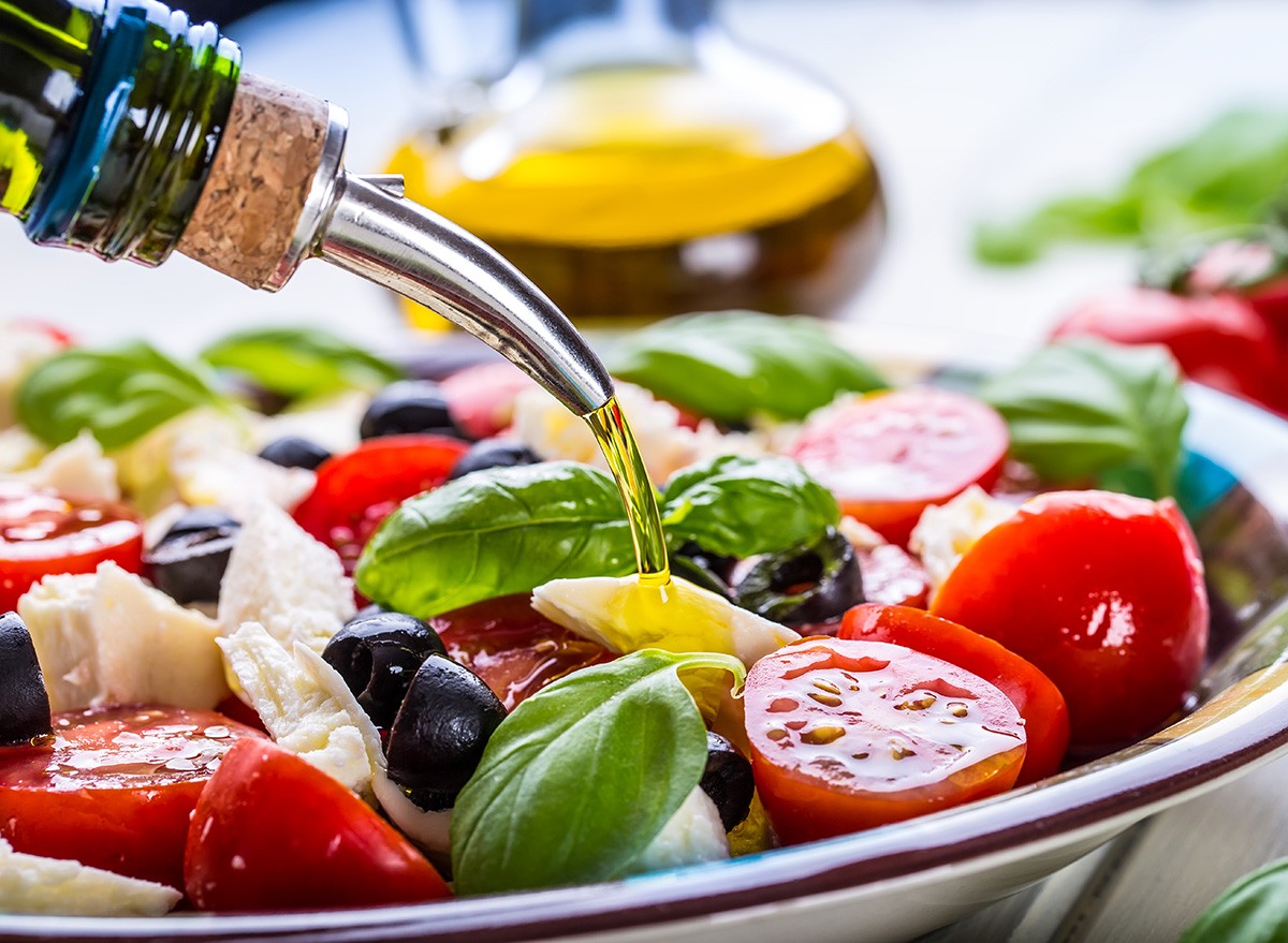 Caprese Italian or Mediterranean salad. Tomato mozzarella basil leaves black olives and olive oil on wooden table.