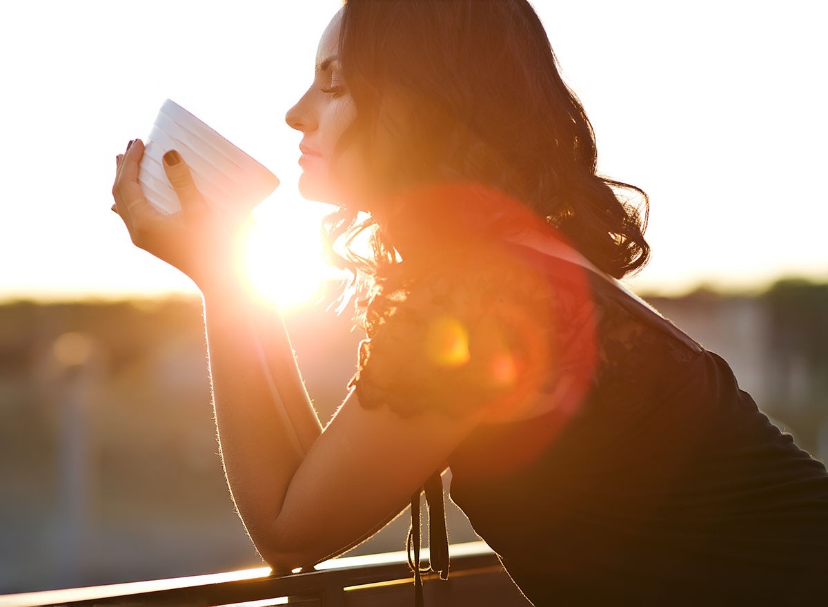 Woman drinking coffee in the sun, outdoor in sunlight light, enjoying her morning coffee.