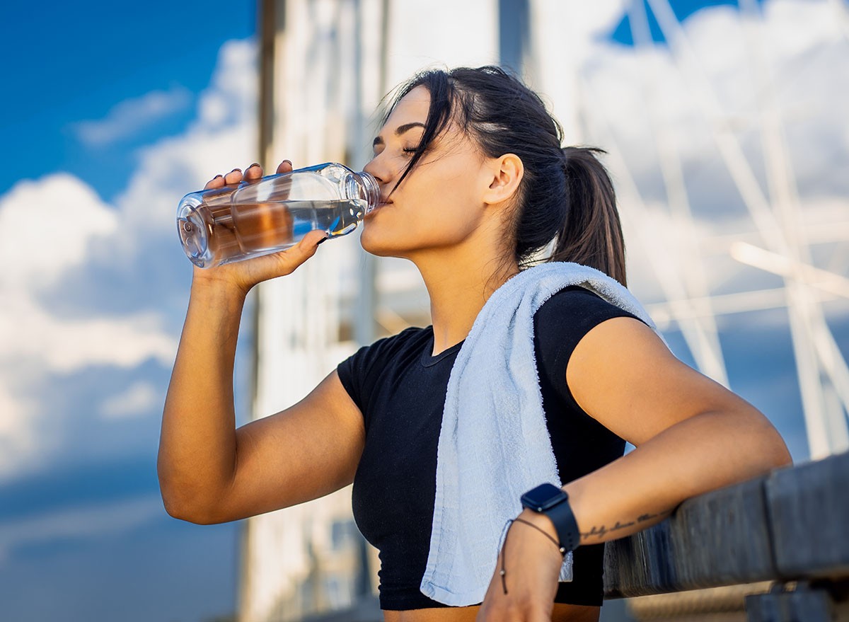 Young woman in black sport outfit resting and drinking water after running.