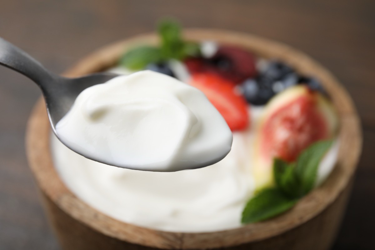 Spoon,With,Tasty,Yogurt,Above,Bowl,On,Table,,Closeup.,Space